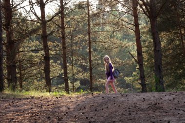 Sırt çantalı sarışın yalnız kız ormanda yürüyor. İnsanlardan uzak temiz havada yürü. Aktif ve sağlıklı yaşam tarzı kavramı.