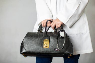 Elinde siyah deri bir doktor çantası olan kadın doktor, doktorluk yapmak için ofise gidiyor.