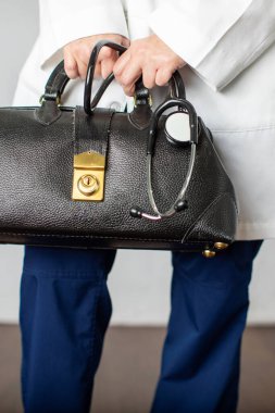 Elinde siyah deri bir doktor çantası olan kadın doktor, doktorluk yapmak için ofise gidiyor.