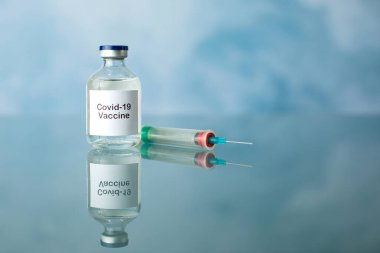 Mavi arka planda şırınga ve eldivenle birlikte Covid-19 Coronavirus aşısı şişesi.