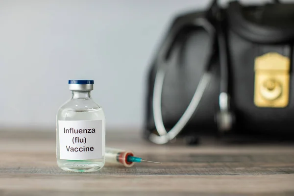 Influenza flu vaccine in a clear vial with a syringe and other medical equipment
