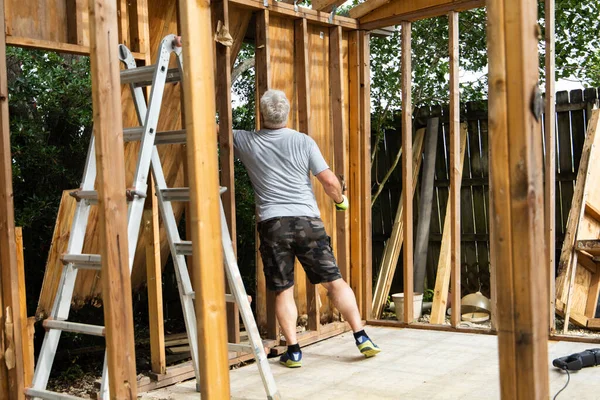 在拆除阶段 一个男人在一个正在腐烂和倒塌的后院拆除了一个旧的棚屋 — 图库照片
