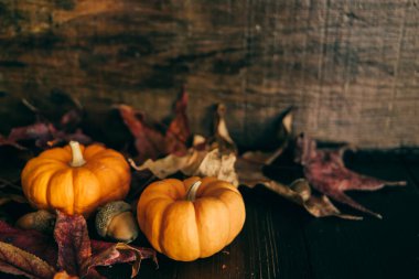 Düşen yapraklarla dolu siyah bir ahşap masa ve Şükran Günü ziyafeti davetiyesi için parlak turuncu bir minyatür balkabağı.