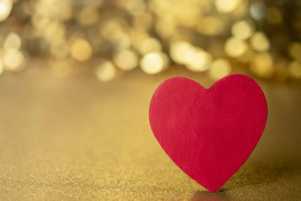 One single red heart  on a gold glitter and sequin background that sparkles and has lots of copy space for love and Valentine\'s Day