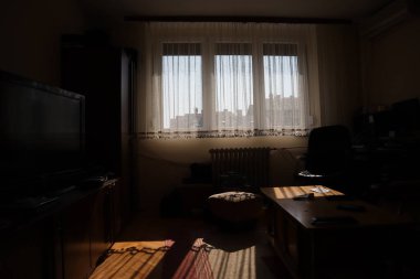 Pencereleri güneşle aydınlanan karanlık oturma odası, loş ışıklandırılmış arka plan çekimleri. Karanlık odadan gelen güneş ışınları arka camı aydınlatırken