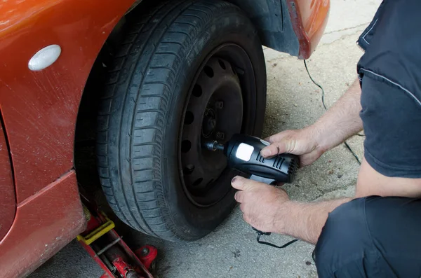 Mechanic changing wheel on car with impact wrench,  man with electric screwdriver changing tire on street close up