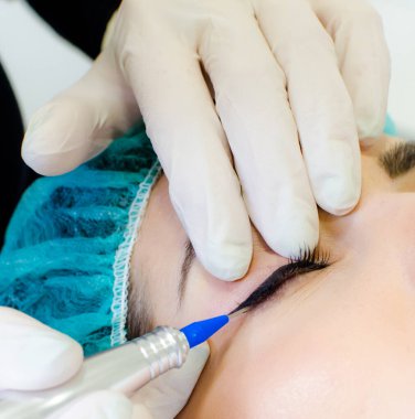 Kalıcı makyaj dövmesi. Kozmetik uzmanı, güzellik salonundaki genç bayana kalıcı makyaj kalemi, göz kalemi ve dövme uyguluyor.