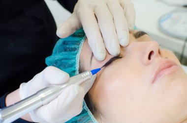 Kalıcı makyaj dövmesi. Kozmetik uzmanı, güzellik salonundaki genç bayana kalıcı makyaj kalemi, göz kalemi ve dövme uyguluyor.