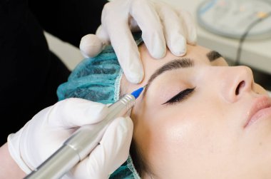 Kalıcı kaş makyajı yapan kozmetolog, güzellik salonundaki genç kadına dövme prosedürü, aşırı yakın çekim.