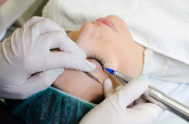 Kalıcı makyaj dövmesi. Kozmetik uzmanı göz kalemi uyguluyor. Güzellik salonunda genç bir kadına göz kalemi dövmesi yaptırıyor. Mankenin arkasından bakıyor.