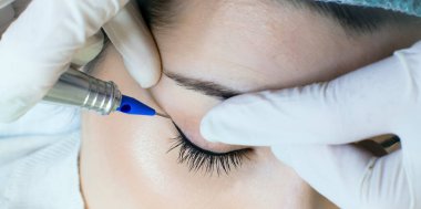 Kalıcı makyaj dövmesi. Kozmetik uzmanı göz kalemi uyguluyor. Güzellik salonunda genç bir kadına göz kalemi dövmesi yaptırıyor.