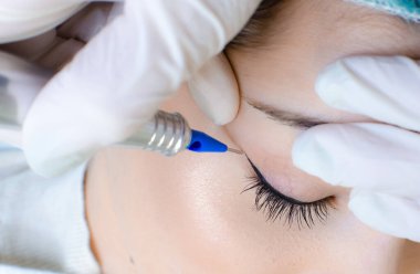 Kalıcı makyaj dövmesi. Kozmetik uzmanı göz kalemi uyguluyor. Güzellik salonunda genç bir kadına göz kalemi dövmesi yaptırıyor.