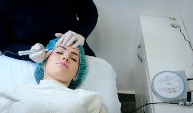 Kalıcı kaş makyajı yapan kozmetikçi. Güzellik salonunda genç bir kadının dövmesi var. Yakın plan. 