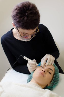 Kalıcı makyaj dövmesi. Gülümseyen Güzellik Uzmanı kalıcı makyaj kalemi sürüyor. Güzellik salonunda genç bir kadına göz kalemi dövmesi yaptırıyor. Kapatın.