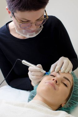 Kalıcı makyaj dövmesi. Gülümseyen Güzellik Uzmanı kalıcı makyaj kalemi sürüyor. Güzellik salonunda genç bir kadına göz kalemi dövmesi yaptırıyor. Kapatın.