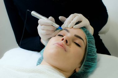 Kalıcı kaş makyajı yapan kozmetikçi. Güzellik salonunda genç bir kadının dövmesi var. Yakın plan. 