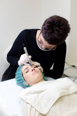 Kalıcı kaş makyajı yapan kozmetikçi. Güzellik salonunda genç bir kadının dövmesi var. Yakın plan. 