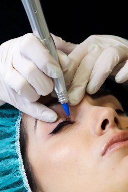 Kalıcı makyaj dövmesi. Kozmetik uzmanı göz kalemi uyguluyor. Güzellik salonunda genç bir kadına göz kalemi dövmesi yaptırıyor.