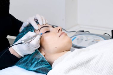 Kozmetik uzmanı kalıcı makyaj kalemi, güzellik salonundaki genç kadına göz kalemi dövmesi uygulaması, iğneli kalıcı makyaj aleti. 