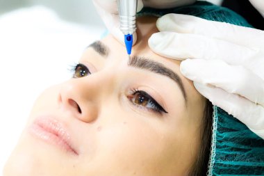 Kalıcı kaş makyajı yapan kozmetolog, güzellik salonundaki genç kadına dövme prosedürü, aşırı yakın çekim.