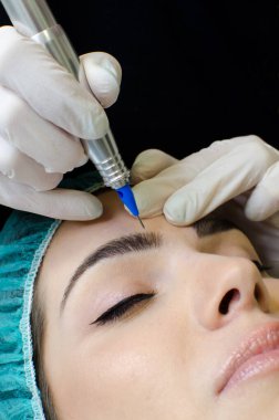 Kalıcı kaş makyajı yapan kozmetikçi, güzellik salonundaki genç kadına dövme prosedürü, aşırı yakın plan, dikey görüntü.