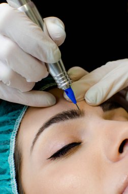 Kalıcı kaş makyajı yapan kozmetikçi, güzellik salonundaki genç kadına dövme prosedürü, aşırı yakın plan, dikey görüntü.