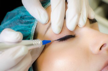 Kalıcı makyaj dövmesi. Kozmetik uzmanı, güzellik salonundaki genç bayana kalıcı makyaj kalemi, göz kalemi ve dövme uyguluyor.