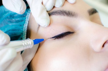 Kalıcı makyaj dövmesi. Kozmetik uzmanı, güzellik salonundaki genç bayana kalıcı makyaj kalemi, göz kalemi ve dövme uyguluyor.