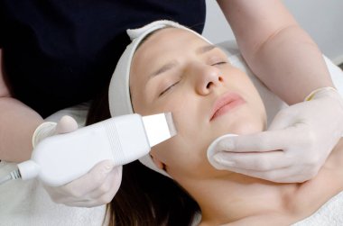 Güzel bir kadın ultrasonik cilt bakımı yaptırıyor, beyaz eldivenli güzellik uzmanı ultrasonik süzgeç tutuyor, güzellik salonunda yüz temizleme prosedürü uyguluyor. Modern ultrasonik cilt ekipmanı.