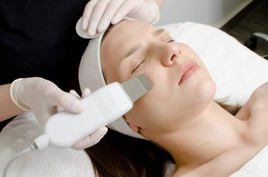 Güzel bir kadın ultrasonik cilt bakımı yaptırıyor, beyaz eldivenli güzellik uzmanı ultrasonik süzgeç tutuyor, güzellik salonunda yüz temizleme prosedürü uyguluyor. Modern ultrasonik cilt ekipmanı.