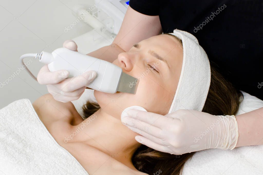 Cosmetologist,beautician in white gloves  making facial treatment with ultrasonic spatula to young woman,face skin scrubber treatment with ultrasonic spatula,facial cleansing procedure in beauty salon