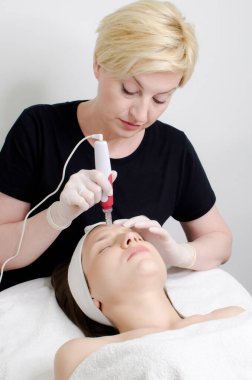 Kadın müşteriye mezoterapi yapmak için maske takan ciddi sarışın bir güzellik uzmanı. Mezoterapi, cilt bakımı, yüz bakımı güzellik salonunda yüz gençleştirme, dikey görüntü.