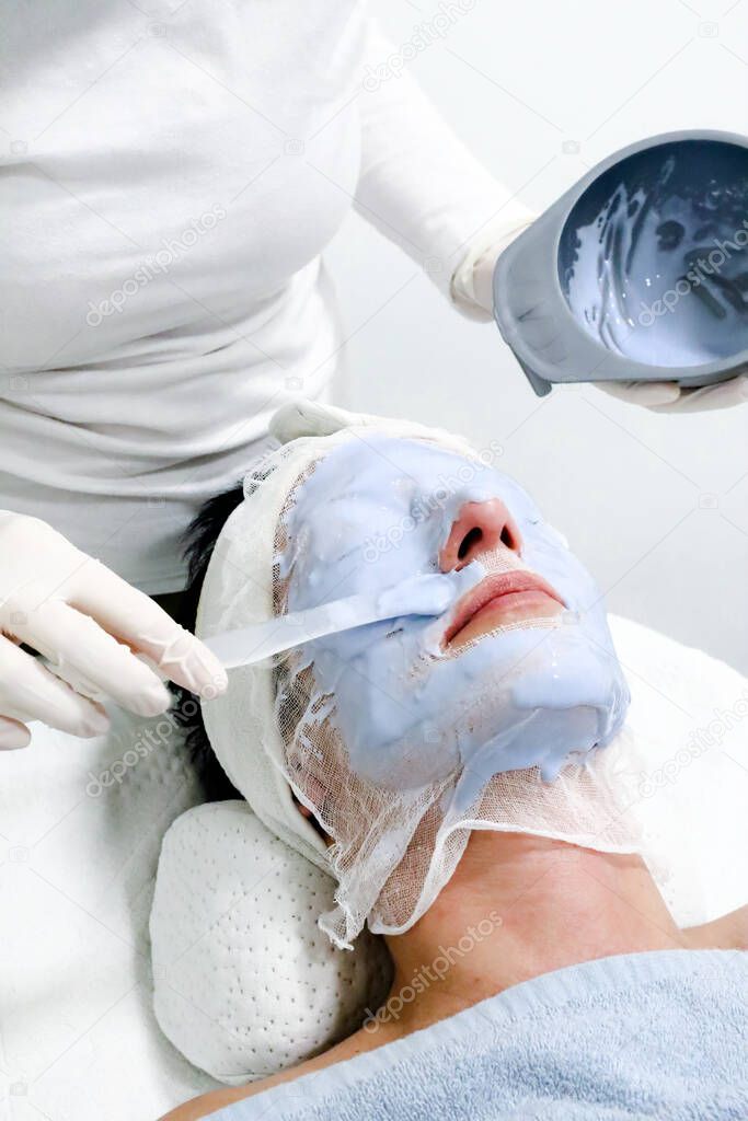 beautician worker applying  cosmetic Caviar peel off mask for facial skin care  to female client in beauty salon 