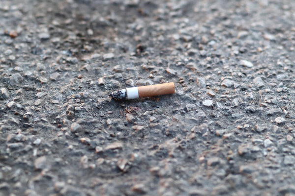 горящий окурок, холостой, изолированный на бетоне. Сигарета на тротуаре, рядом, вид сверху
 