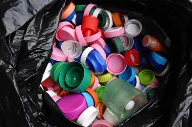 Siyah plastik torba içinde çok renkli şişe kapakları, üst görünümü geri dönüşüme hazır. 
