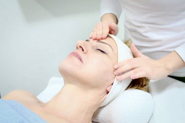 Güzellik uzmanı güzellik salonundaki kadın kostümcünün yüzüne nazikçe masaj yapıyor.