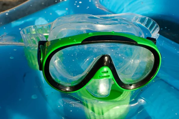 green diving mask for kids on blue sea mattress on sunny day at the beach close up