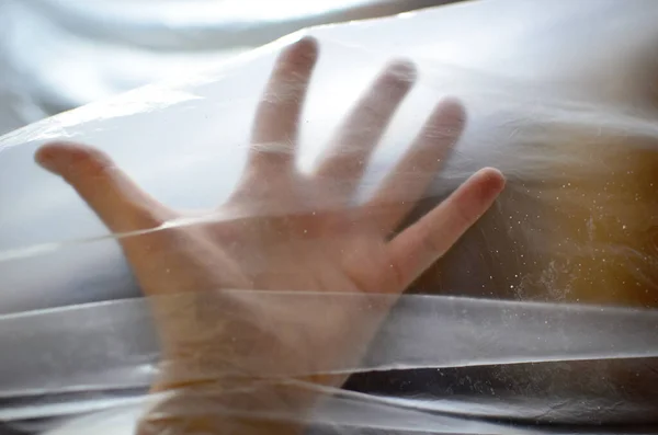 Silhouette of a hand behind transparent plastic foil, indoor, reaching out behind the transparent plastic