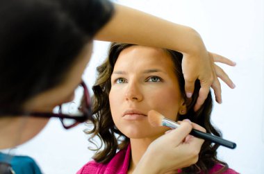 Makyaj sanatçısı model yüzünü fırçalamaya çalışıyor. Güzellik stüdyosunun içinde genç bir kadının portresi. Kozmetik fırçayla allık süren Güzel Genç Kadın Modeli 'nin kapanışı