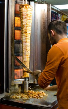 Istanbul, Turkey, March 08, 2019:  worker at fast food restaurant cutting doner kebab on rotating vertical spit, traditional street food, night shot  clipart
