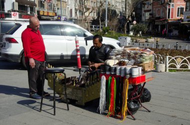 İstanbul, Türkiye, 10 Mart 2019: Ayakkabı imalatçısı İstanbul caddesinde ayakkabı tamir ederken, kırmızı gömlekli müşteri ayakkabı işçisi, güneşli bir günde açık havada geleneksel el işi, küçük işletme sahibi