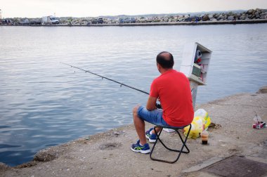 Nea Mudania, Chalkidiki yarımadası, Yunanistan, 12 Ağustos 2018: Sabahın erken saatlerinde kırmızılı adam Nea Moudania limanında, kahve içip balık tutuyor. 