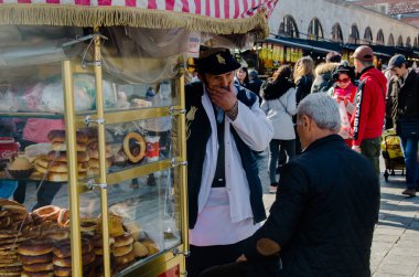 İstanbul, Türkiye, 07 Mart 2019: Geleneksel takım elbiseli Türk simidi satıcısı güneşli bir günde Eminonu 'daki Mısır Çarşısı veya Baharat Pazarı önünde yaşlı bir adamla konuşuyor