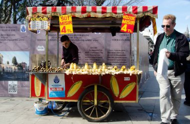 İstanbul, Türkiye, 07 Mart 2019: İstanbul 'da sokaktan geçen güneş gözlüğü ve plastik torba takan bir adamla haşlanmış ve ızgara mısır satan geleneksel sokak satıcıları