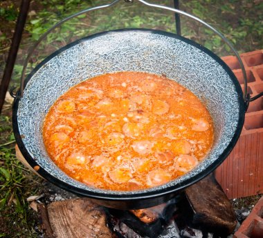 Fasulye ve sosis yemeği doğada kamp ateşinde büyük metal çaydanlıkta pişiyor.