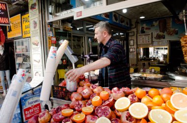 • Türkiye, Mart 08.2019: Meyve sıkacağı ile satıcı taze meyve suyu, çiğ portakal ve nar yığını sokak pazarında, güneşli İstanbul sokaklarında açık havada