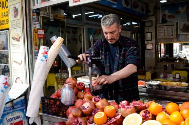 • Türkiye, Mart 08.2019: Meyve sıkacağı ile satıcı taze meyve suyu, çiğ portakal ve nar yığını sokak pazarında, güneşli İstanbul sokaklarında açık havada
