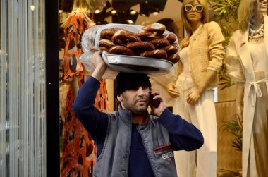 İstanbul, Türkiye, 07 Mart 2019: Bir adam mağazanın önünde dikilip kendi telefonuyla konuşurken, diğer elinde Türk simidi dolu metal bir tabak tutuyor. 
