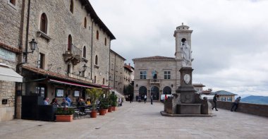 San Marino, İtalya, 09 Mayıs 2019 San Marino merkez meydanı. Sokak kahveli Özgürlük Sarayı ve Heykeli ve bulutlu bir günde yürüyen turistler. 