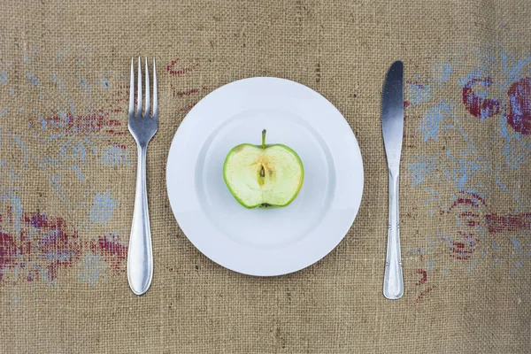 Μισό μπαγιάτικο πράσινο μήλο σε λευκό πιάτο με πιρούνι και μαχαίρι. — Φωτογραφία Αρχείου